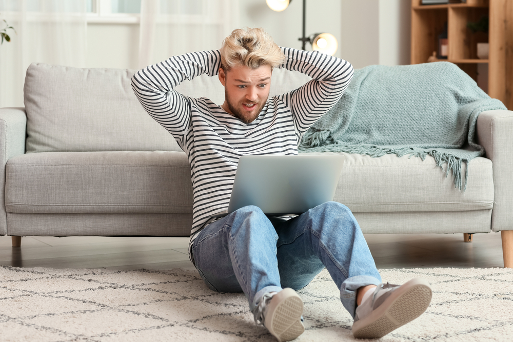 A MAN SITTING AT A LAPTOP WITH A STRESSED EXPRESSION DUE TO NO SEO RESULTS